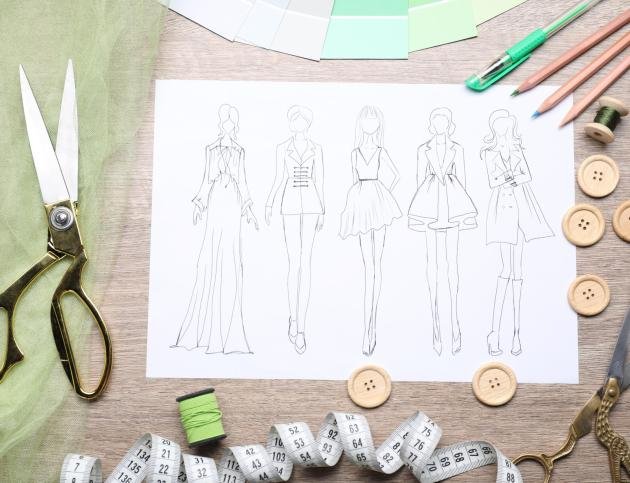 Sketch of stylish clothes and other fashion designer`s supplies on wooden table, flat lay